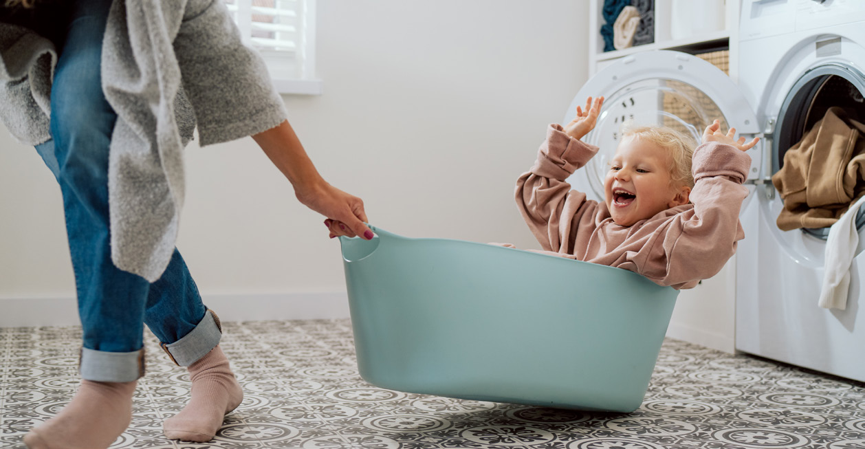Moeder en lachend kind in wasmand in moderne wasruimte — comfort thuis dankzij PVT-systeem